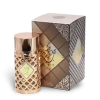 Ard Al Zaafaran Jazzab Gold Eau De Parfum 100ml — A gold-toned perfume bottle with a diamond-patterned cage sits next to its matching patterned box on a white background. | Ard Al Zaafaran Jazzab Gold Eau De Parfum 100ml — Botol minyak wangi berwarna emas dengan sangkar bermotif berlian duduk bersebelahan dengan kotak