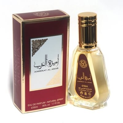 Ard Al Zaafaran Ameerat Al Arab Princess of Arabia 50ml — A red and gold perfume box stands next to a clear glass perfume bottle with a gold cap and a red label. | Ard Al Zaafaran Ameerat Al Arab Princess of Arabia 50ml — Kotak minyak wangi merah dan emas berdiri di sebelah botol minyak wangi kaca jernih dengan