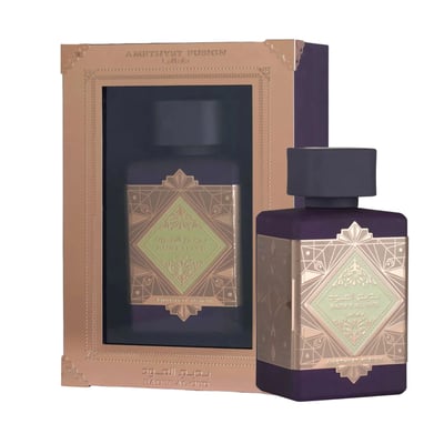 Lattafa Bade'e Al Oud Amethyst Fusion 100ml — A purple perfume bottle with a gold geometric label sits next to its matching box, which has a gold frame and a window showing the bottle inside. | Lattafa Bade'e Al Oud Amethyst Fusion 100ml — Botol minyak wangi ungu dengan label geometri emas duduk bersebelahan dengan