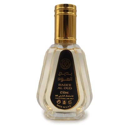 Ard Al Zaafaran Badee Al Oud Eau De Parfum 50ml — Black and gold geometric patterned box next to a clear glass perfume bottle with a gold cap, on a white background. | Ard Al Zaafaran Badee Al Oud Eau De Parfum 50ml — Kotak hitam dan emas bercorak geometri di sebelah botol minyak wangi kaca jernih bertudung emas, di
