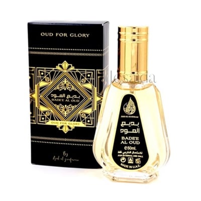 Ard Al Zaafaran Badee Al Oud Eau De Parfum 50ml — Black and gold geometric patterned box next to a clear glass perfume bottle with a gold cap, on a white background. | Ard Al Zaafaran Badee Al Oud Eau De Parfum 50ml — Kotak hitam dan emas bercorak geometri di sebelah botol minyak wangi kaca jernih bertudung emas, di