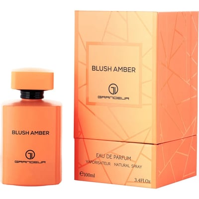 Grandeur Blush Amber 100ml — An orange perfume bottle and its matching orange box with geometric patterns, displayed side-by-side against a white background. | Grandeur Blush Amber 100ml — Botol minyak wangi oren dan kotak orennya yang sepadan dengan corak geometri, dipaparkan bersebelahan di atas latar belakang putih.