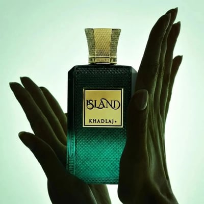 Khadlaj Island Extrait de Parfum — A perfume bottle with a dark green gradient and a gold textured cap sits next to its matching box, which features a white background with abstract green and gold marbling and palm leaf motifs. | Khadlaj Island Extrait de Parfum — Botol minyak wangi dengan gradien hijau gelap dan