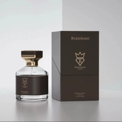 Bujairami Kingsman — A clear glass perfume bottle with a black leather band and gold accents sits next to its dark brown