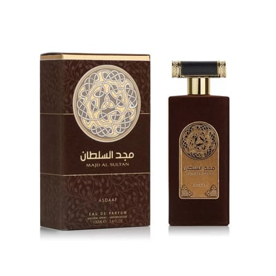 Asdaaf Majd Al Sultan — A dark brown velvet-textured perfume bottle with a gold and black cap stands next to its matching brown box, both featuring a circular Celtic knot design. | Asdaaf Majd Al Sultan — Botol minyak wangi bertekstur baldu coklat gelap dengan penutup emas dan hitam berdiri di sebelah kotak coklat