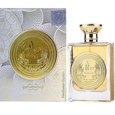 Ard Al Zaafaran Mithqal 100ml — A clear glass perfume bottle with gold liquid and a circular gold emblem, next to its white and gold patterned box with a matching emblem. | Ard Al Zaafaran Mithqal 100ml — Botol minyak wangi kaca jernih dengan cecair emas dan lambang emas bulat, bersebelahan dengan kotak corak putih
