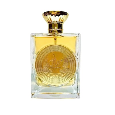 Ard Al Zaafaran Mithqal 100ml — A clear glass perfume bottle with gold liquid and a circular gold emblem, next to its white and gold patterned box with a matching emblem. | Ard Al Zaafaran Mithqal 100ml — Botol minyak wangi kaca jernih dengan cecair emas dan lambang emas bulat, bersebelahan dengan kotak corak putih