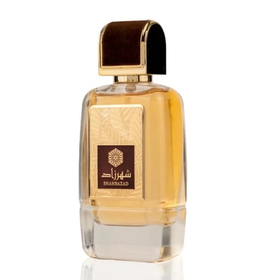 Ard Al Zaafaran Shahrazad Eau De Parfum — A white box with gold leaf pattern and a clear glass perfume bottle with gold accents and amber liquid, set against a white background. | Ard Al Zaafaran Shahrazad Eau De Parfum — Kotak putih dengan corak daun emas dan botol minyak wangi kaca jernih dengan aksen emas dan