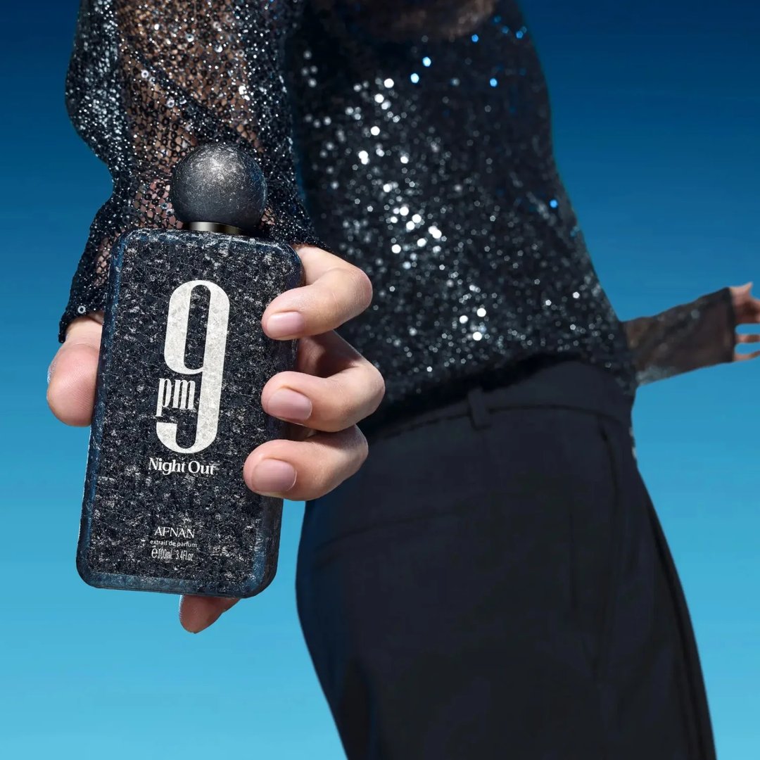 Afnan 9 PM Night Out Extrait de Parfum — A black textured perfume bottle with a dark textured cap stands next to its matching black textured box, both featuring a large white '9 PM Night Out' logo. | Afnan 9 PM Night Out Extrait de Parfum — Botol minyak wangi bertekstur hitam dengan penutup bertekstur gelap berdiri di