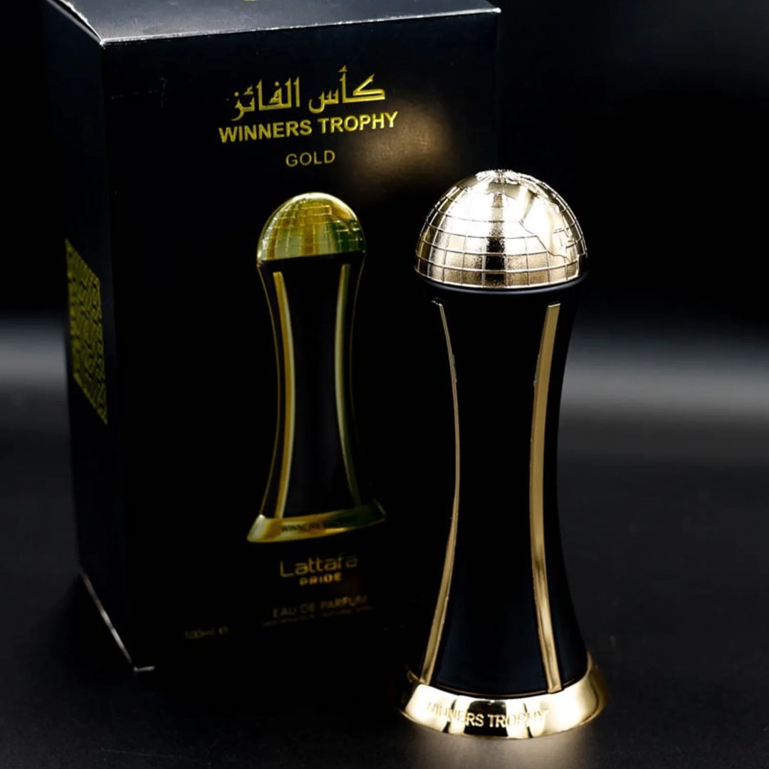 Lattafa Pride Al Khas Winners Trophy Gold 100ml — A black perfume box with gold Arabic and English text, and a gold-capped black perfume bottle shaped like an hourglass, displayed on a white background. | Lattafa Pride Al Khas Winners Trophy Gold 100ml — Kotak minyak wangi hitam dengan teks Arab dan Inggeris emas, dan