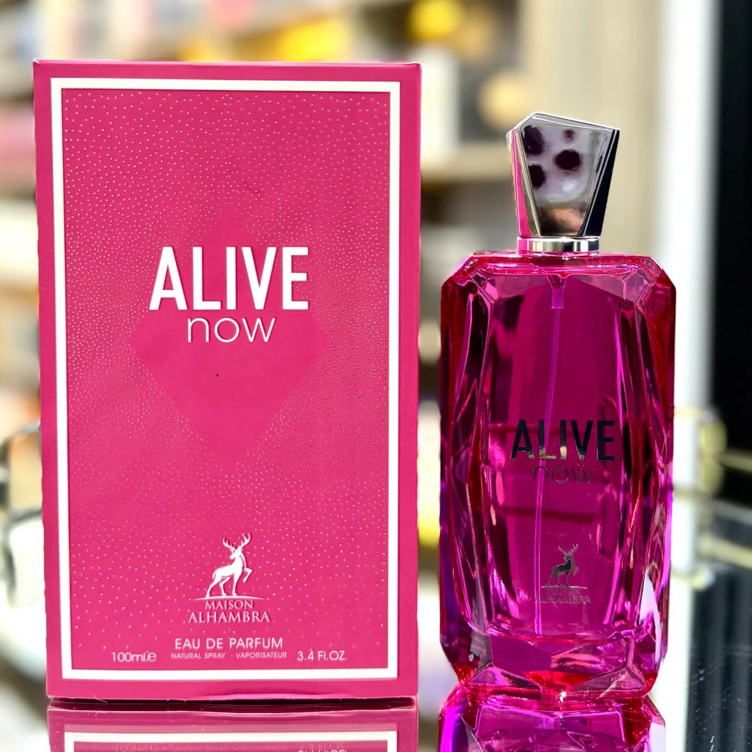 Maison Alhambra Alive Now — A bright pink faceted glass perfume bottle with a silver geometric cap stands next to its matching pink box, which features a dotted pattern and the brand logo. | Maison Alhambra Alive Now — Botol kaca berwarna merah jambu terang berbentuk faset dengan penutup geometri perak berdiri di