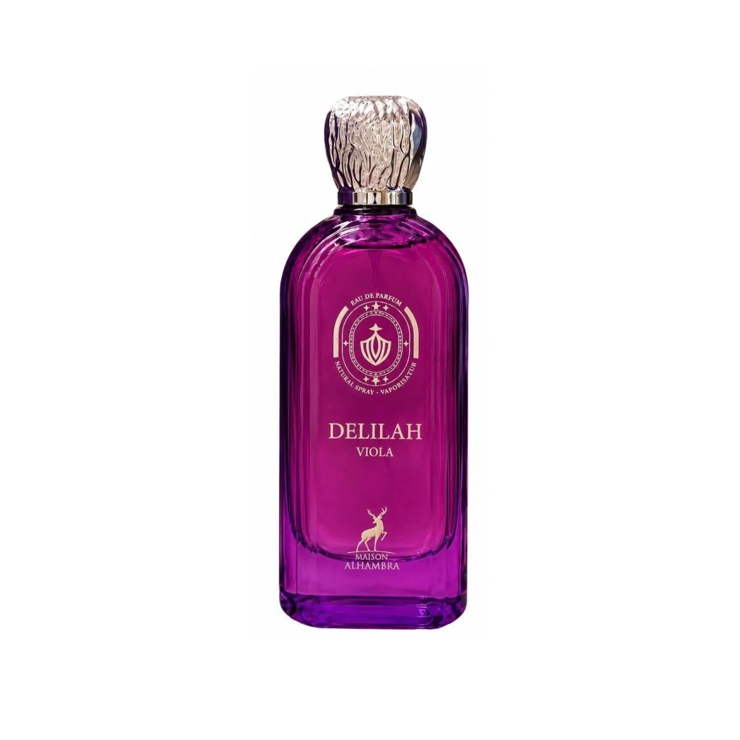 Maison Alhambra Delilah Viola 100ml — A purple glass perfume bottle with a gold cap stands next to its matching purple box, both featuring gold embossed details and a deer logo. | Maison Alhambra Delilah Viola 100ml — Botol kaca ungu berdiri di sebelah kotak ungu sepadan, kedua-duanya menampilkan butiran emas timbul