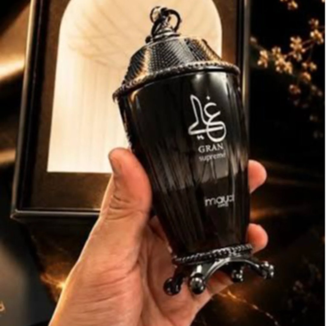 Zimaya Ghali Imperial Eau De Parfum — A dark grey textured box with a building facade pattern stands next to a dark, fluted perfume bottle with a tassel. | Zimaya Ghali Imperial Eau De Parfum — Kotak kelabu gelap bertekstur dengan corak fasad bangunan berdiri di sebelah botol minyak wangi gelap berlekuk dengan juntai.