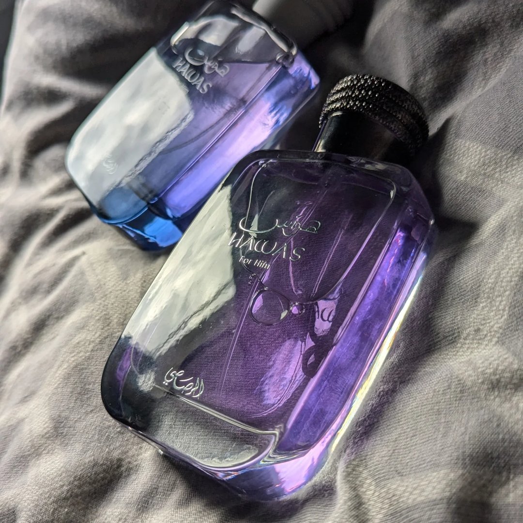 Rasasi Hawas For Him Eau De Parfum 100ml by Rasasi — A clear glass perfume bottle with purple liquid and a textured grey cap sits next to a black product box with a snakeskin pattern label. | Rasasi Hawas For Him Eau De Parfum 100ml by Rasasi — Botol minyak wangi kaca jernih dengan cecair ungu dan penutup kelabu