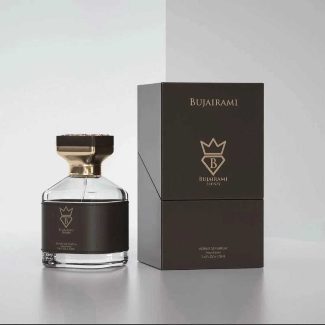 Bujairami Kingsman — A clear glass perfume bottle with a black leather band and gold accents sits next to its dark brown
