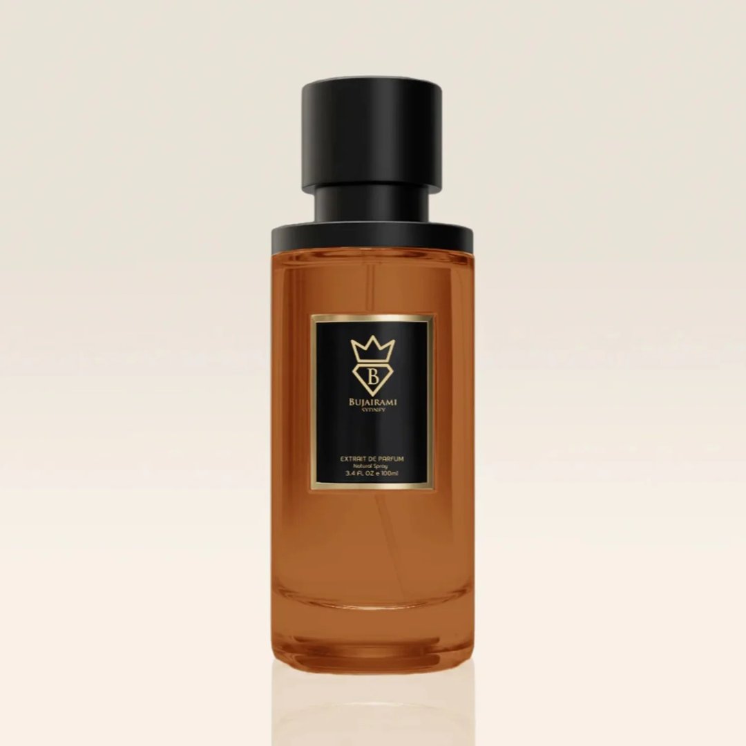 Bujairami Legacy by Bujairami 100ml Extrait — An amber-colored glass perfume bottle with a black cap and a black label featuring gold text and a gold crest. | Bujairami Legacy by Bujairami 100ml Extrait — Botol kaca berwarna ambar dengan penutup hitam dan label hitam yang menampilkan teks emas dan lambang emas.