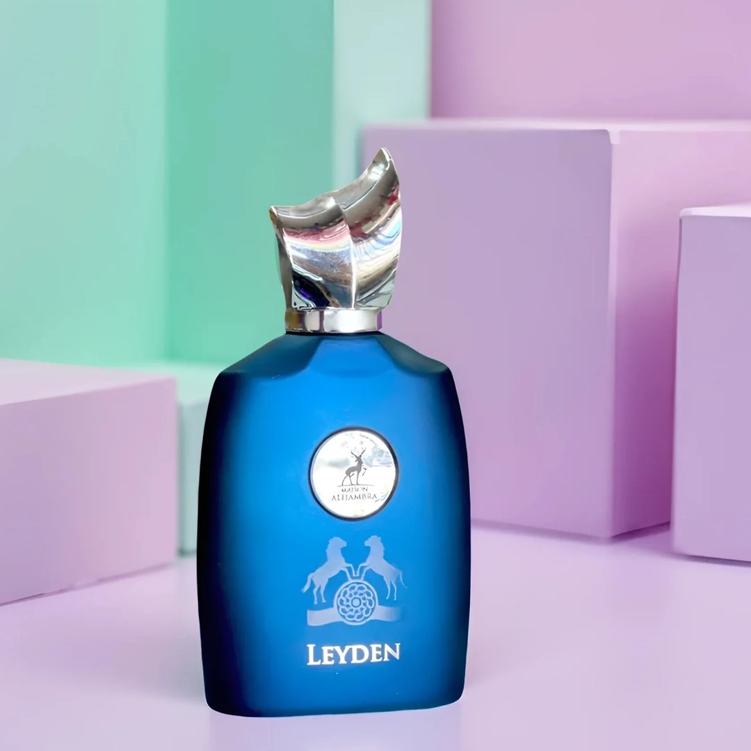 Maison Alhambra Leyden Eau De Parfum — A dark blue perfume bottle and its matching striped box are displayed side-by-side against a white background. The box features two white horses and a circular emblem. | Maison Alhambra Leyden Eau De Parfum — Botol minyak wangi biru gelap dan kotaknya yang berjalur dipamerkan