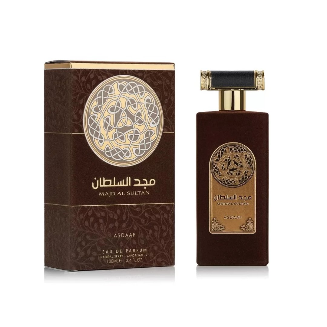 Asdaaf Majd Al Sultan — A dark brown velvet-textured perfume bottle with a gold and black cap stands next to its matching brown box, both featuring a circular Celtic knot design. | Asdaaf Majd Al Sultan — Botol minyak wangi bertekstur baldu coklat gelap dengan penutup emas dan hitam berdiri di sebelah kotak coklat