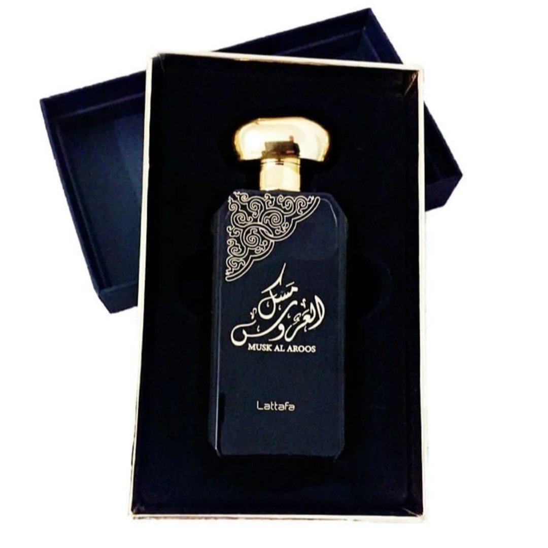 Lattafa Musk Al Aroos by Lattafa 80ml EDP — A black perfume box with gold ornate cutouts and Arabic calligraphy sits next to a dark glass perfume bottle with a gold cap and matching ornate design. | Lattafa Musk Al Aroos by Lattafa 80ml EDP — Kotak minyak wangi hitam dengan potongan berukir emas dan kaligrafi Arab