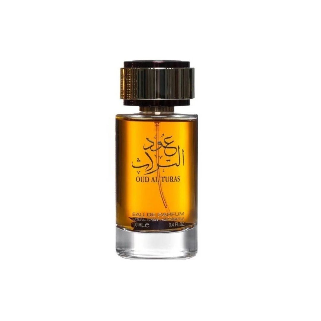 Ard Al Zaafaran Oud Al Turas — A clear glass perfume bottle with golden cap and a dark dried plant inside, next to a gold and maroon ornate box. | Botol minyak wangi kaca jernih dengan penutup emas dan tumbuhan kering gelap di dalamnya, bersebelahan dengan kotak berhias emas dan merah marun.