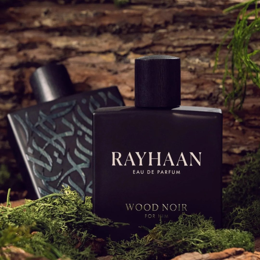 Rayhaan Woody Noir Eau De Parfum — A dark grey bottle of Rayhaan Woody Noir Eau De Parfum for him sits next to its matching dark grey box with embossed wood grain texture. | Rayhaan Woody Noir Eau De Parfum — Botol Rayhaan Woody Noir Eau De Parfum kelabu gelap untuk lelaki terletak di sebelah kotak kelabu gelap yang