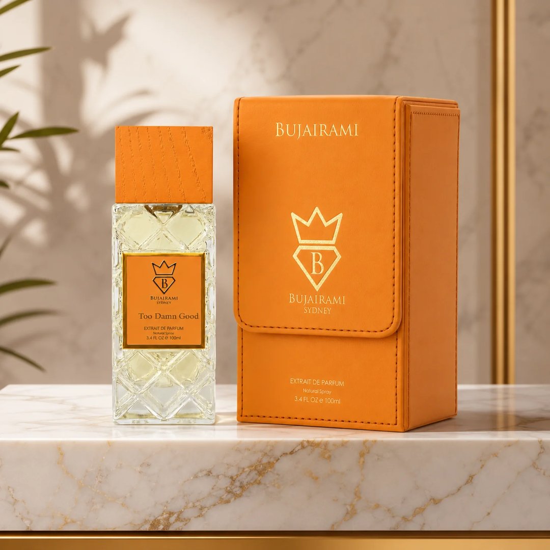 Bujairami Too Damn Good — Clear faceted glass perfume bottle with wooden cap next to orange leather box with gold logo