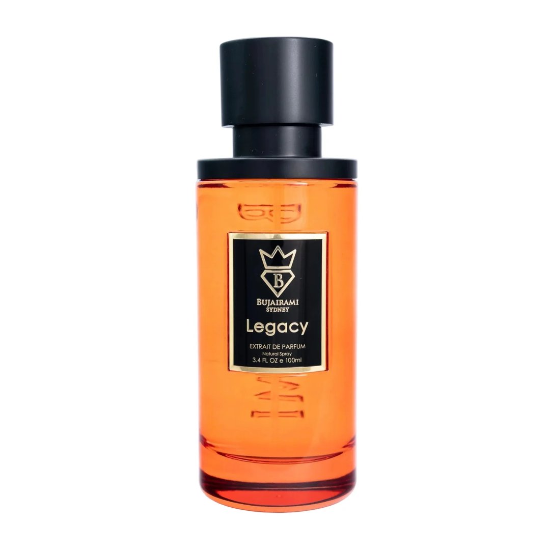 Bujairami Legacy by Bujairami 100ml Extrait — An amber-colored glass perfume bottle with a black cap and a black label featuring gold text and a gold crest. | Bujairami Legacy by Bujairami 100ml Extrait — Botol kaca berwarna ambar dengan penutup hitam dan label hitam yang menampilkan teks emas dan lambang emas.