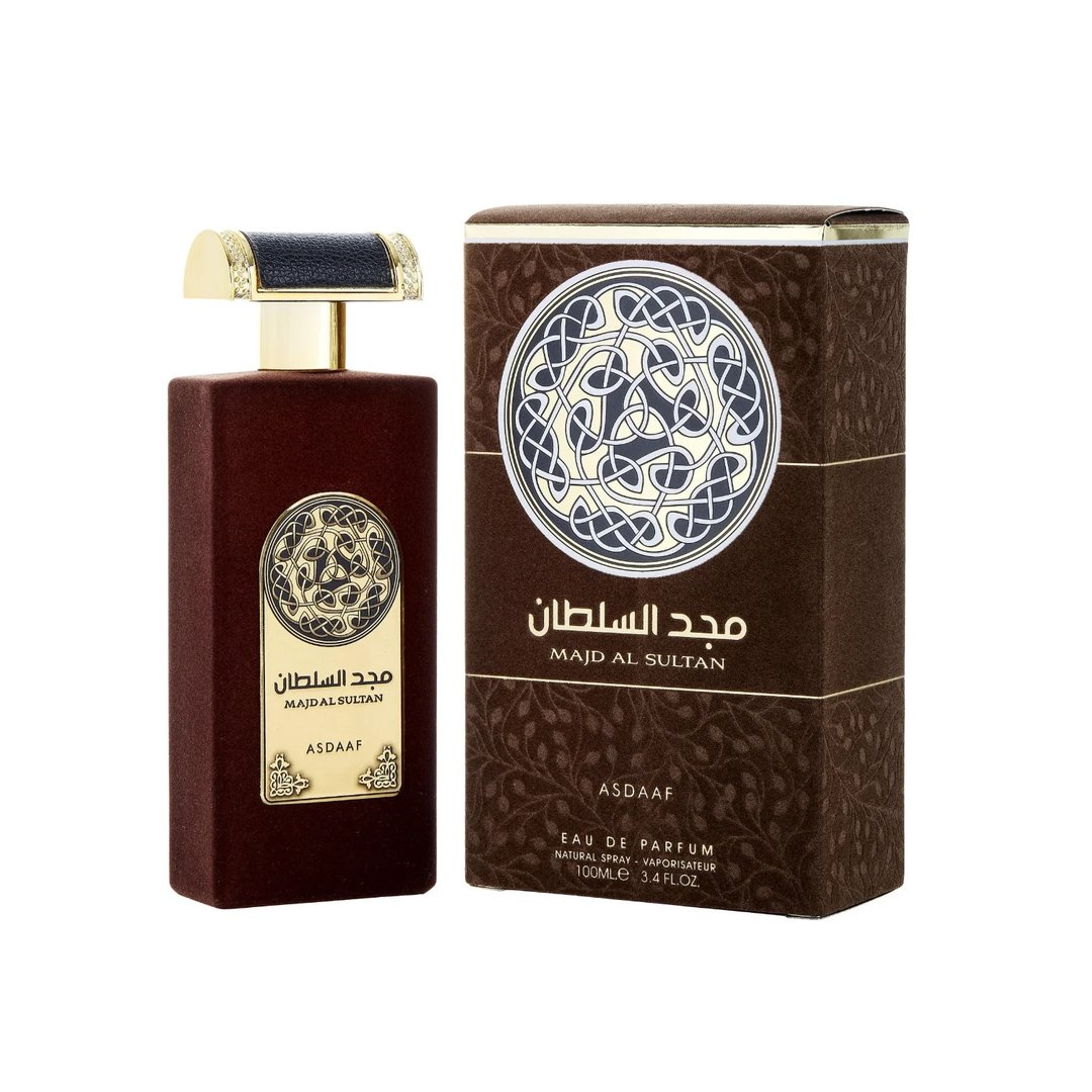 Asdaaf Majd Al Sultan — A dark brown velvet-textured perfume bottle with a gold and black cap stands next to its matching brown box, both featuring a circular Celtic knot design. | Asdaaf Majd Al Sultan — Botol minyak wangi bertekstur baldu coklat gelap dengan penutup emas dan hitam berdiri di sebelah kotak coklat