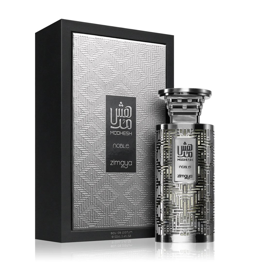 Zimaya Modhesh Noble 100ml — A silver patterned gift box stands next to a matching silver patterned perfume bottle with a metallic cap, both on a white background. | Zimaya Modhesh Noble 100ml — Kotak hadiah bercorak perak berdiri di sebelah botol minyak wangi bercorak perak yang sepadan dengan penutup logam