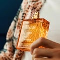 Rayhaan Adonis Icarus Perfume — A gold embossed box sits next to a square amber glass perfume bottle with a gold cap, both featuring intricate embossed patterns. | Rayhaan Adonis Icarus Perfume — Kotak emas bertekstur duduk bersebelahan botol minyak wangi kaca berwarna ambar berbentuk segi empat dengan penutup emas