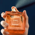 Rayhaan Adonis Icarus Perfume — A gold embossed box sits next to a square amber glass perfume bottle with a gold cap, both featuring intricate embossed patterns. | Rayhaan Adonis Icarus Perfume — Kotak emas bertekstur duduk bersebelahan botol minyak wangi kaca berwarna ambar berbentuk segi empat dengan penutup emas