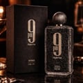 Afnan 9 PM Night Out Extrait de Parfum — A black textured perfume bottle with a dark textured cap stands next to its matching black textured box, both featuring a large white '9 PM Night Out' logo. | Afnan 9 PM Night Out Extrait de Parfum — Botol minyak wangi bertekstur hitam dengan penutup bertekstur gelap berdiri di