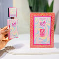 Lattafa Ajwad Pink 2 Pink Creamy Elixir EDP — Pink rectangular bottle with a colorful wavy pattern, topped with a smaller black cap featuring a similar wavy design and gold accents.