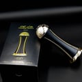 Lattafa Pride Al Khas Winners Trophy Gold 100ml — A black perfume box with gold Arabic and English text, and a gold-capped black perfume bottle shaped like an hourglass, displayed on a white background. | Lattafa Pride Al Khas Winners Trophy Gold 100ml — Kotak minyak wangi hitam dengan teks Arab dan Inggeris emas, dan
