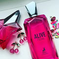 Maison Alhambra Alive Now — A bright pink faceted glass perfume bottle with a silver geometric cap stands next to its matching pink box, which features a dotted pattern and the brand logo. | Maison Alhambra Alive Now — Botol kaca berwarna merah jambu terang berbentuk faset dengan penutup geometri perak berdiri di