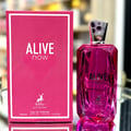 Maison Alhambra Alive Now — A bright pink faceted glass perfume bottle with a silver geometric cap stands next to its matching pink box, which features a dotted pattern and the brand logo. | Maison Alhambra Alive Now — Botol kaca berwarna merah jambu terang berbentuk faset dengan penutup geometri perak berdiri di