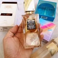 Lattafa Ana Abiyedh Leather 60ml by Lattafa Perfumes — A white perfume box with gold Arabic calligraphy and a clear glass bottle with gold accents and a dark brown cap, displayed side-by-side. | Lattafa Ana Abiyedh Leather 60ml by Lattafa Perfumes — Kotak minyak wangi putih dengan kaligrafi Arab emas dan botol kaca