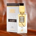 Lattafa Ana Abiyedh Leather 60ml by Lattafa Perfumes — A white perfume box with gold Arabic calligraphy and a clear glass bottle with gold accents and a dark brown cap, displayed side-by-side. | Lattafa Ana Abiyedh Leather 60ml by Lattafa Perfumes — Kotak minyak wangi putih dengan kaligrafi Arab emas dan botol kaca