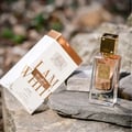 Lattafa Ana Abiyedh Poudree by Lattafa 60ml — A white perfume box with gold accents and Arabic calligraphy stands next to a clear glass perfume bottle with a gold cap and intricate gold detailing on the bottle. | Lattafa Ana Abiyedh Poudree by Lattafa 60ml — Kotak minyak wangi putih dengan aksen emas dan kaligrafi