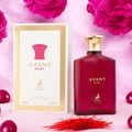 Maison Alhambra Avant Ruby Eau De Parfum 100ml — A bright pink glass perfume bottle with a gold textured cap stands next to its white and gold patterned box, both featuring the Avant Ruby branding and a deer logo. | Maison Alhambra Avant Ruby Eau De Parfum 100ml — Botol kaca berwarna merah jambu terang dengan penutup