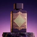 Lattafa Bade'e Al Oud Amethyst Fusion 100ml — A purple perfume bottle with a gold geometric label sits next to its matching box, which has a gold frame and a window showing the bottle inside. | Lattafa Bade'e Al Oud Amethyst Fusion 100ml — Botol minyak wangi ungu dengan label geometri emas duduk bersebelahan dengan