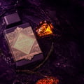 Lattafa Bade'e Al Oud Amethyst Fusion 100ml — A purple perfume bottle with a gold geometric label sits next to its matching box, which has a gold frame and a window showing the bottle inside. | Lattafa Bade'e Al Oud Amethyst Fusion 100ml — Botol minyak wangi ungu dengan label geometri emas duduk bersebelahan dengan