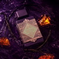 Lattafa Bade'e Al Oud Amethyst Fusion 100ml — A purple perfume bottle with a gold geometric label sits next to its matching box, which has a gold frame and a window showing the bottle inside. | Lattafa Bade'e Al Oud Amethyst Fusion 100ml — Botol minyak wangi ungu dengan label geometri emas duduk bersebelahan dengan