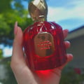 Maison Alhambra Baroque Rouge Extrait 100ml by Maison Alhambra — Red faceted glass perfume bottle with gold cap next to a red and gold ornate box with a bird and deer motif | Maison Alhambra Baroque Rouge Extrait 100ml by Maison Alhambra — Botol kaca merah berfaset dengan penutup emas di sebelah kotak merah dan emas