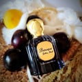 Maison Alhambra Baroque Satin Oud 100ml — A dark glass perfume bottle with a gold textured cap sits next to its matching dark box with gold geometric patterns. | Maison Alhambra Baroque Satin Oud 100ml — Botol minyak wangi kaca gelap dengan penutup bertekstur emas terletak di sebelah kotak gelapnya dengan corak