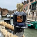 Maison Alhambra Baroque Satin Oud 100ml — A dark glass perfume bottle with a gold textured cap sits next to its matching dark box with gold geometric patterns. | Maison Alhambra Baroque Satin Oud 100ml — Botol minyak wangi kaca gelap dengan penutup bertekstur emas terletak di sebelah kotak gelapnya dengan corak