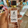 Maison Alhambra Chic Velvet Pink Secret for Women 100ml — A pink cylindrical box stands next to a clear glass perfume bottle with a black cap and gold accents. The box and bottle label feature a deer silhouette and text. | Maison Alhambra Chic Velvet Pink Secret for Women 100ml — Kotak silinder merah jambu berdiri di