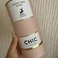 Maison Alhambra Chic Velvet Pink Secret for Women 100ml — A pink cylindrical box stands next to a clear glass perfume bottle with a black cap and gold accents. The box and bottle label feature a deer silhouette and text. | Maison Alhambra Chic Velvet Pink Secret for Women 100ml — Kotak silinder merah jambu berdiri di