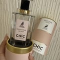 Maison Alhambra Chic Velvet Pink Secret for Women 100ml — A pink cylindrical box stands next to a clear glass perfume bottle with a black cap and gold accents. The box and bottle label feature a deer silhouette and text. | Maison Alhambra Chic Velvet Pink Secret for Women 100ml — Kotak silinder merah jambu berdiri di