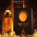 Paris Corner Daar Al Oud Intense 100ml — Black box with gold sunburst and Arabic script next to a glass perfume bottle with gold cap and matching design | Paris Corner Daar Al Oud Intense 100ml — Kotak hitam dengan pancaran matahari emas dan tulisan Arab di sebelah botol minyak wangi kaca dengan penutup emas dan reka